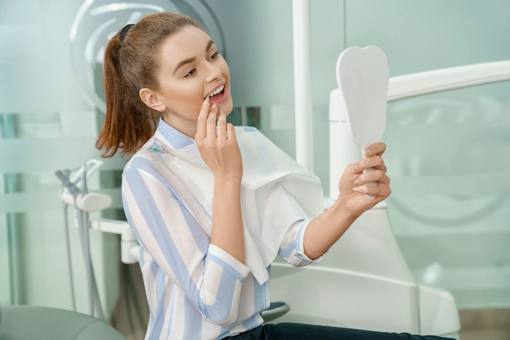 Woman looking at mirror and enjoying smile in dental office